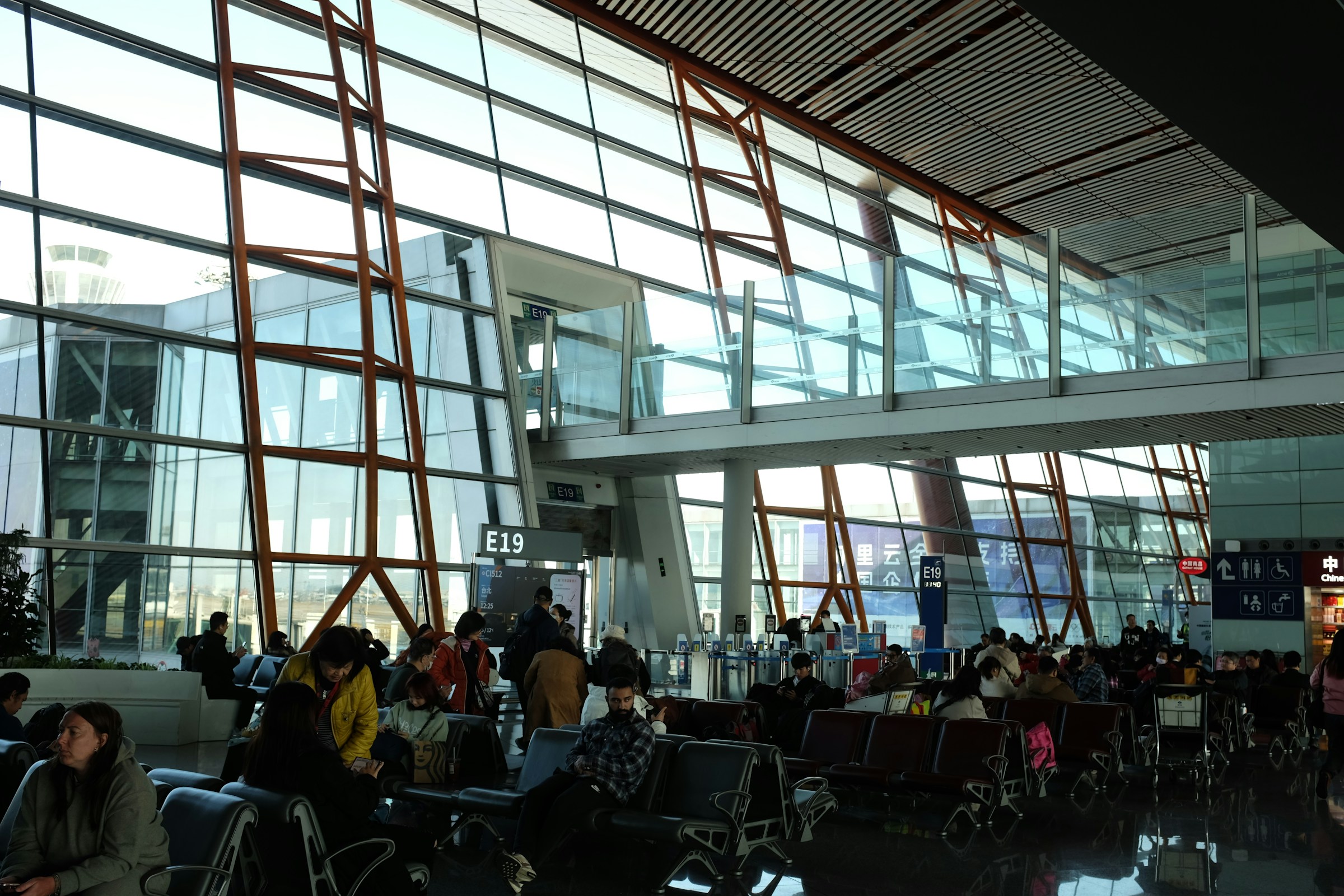 Travellers waiting at a departure gate in a terminal with tall windows